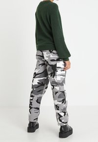 Pull en maille verte à manches longues associé à un pantalon cargo en camouflage gris avec des motifs noirs et blancs. Des chaussures à plateforme noires complètent le look.