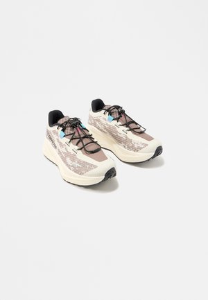 Par de zapatillas de correr deportivas beige y marrones con suelas negras, cordones negros y detalles en azul y rosa, sobre un fondo blanco liso.