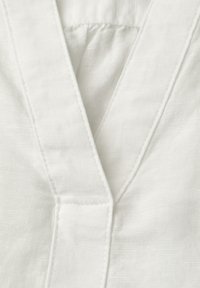 Gros plan sur un tissu blanc présentant un décolleté en V avec des coutures visibles et un tissage texturé.