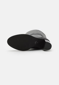 Botte noire mi-mollet en cuir lisse, avec des coutures décoratives et une semelle plate. Comprend une étiquette de taille à l'intérieur de la semelle.