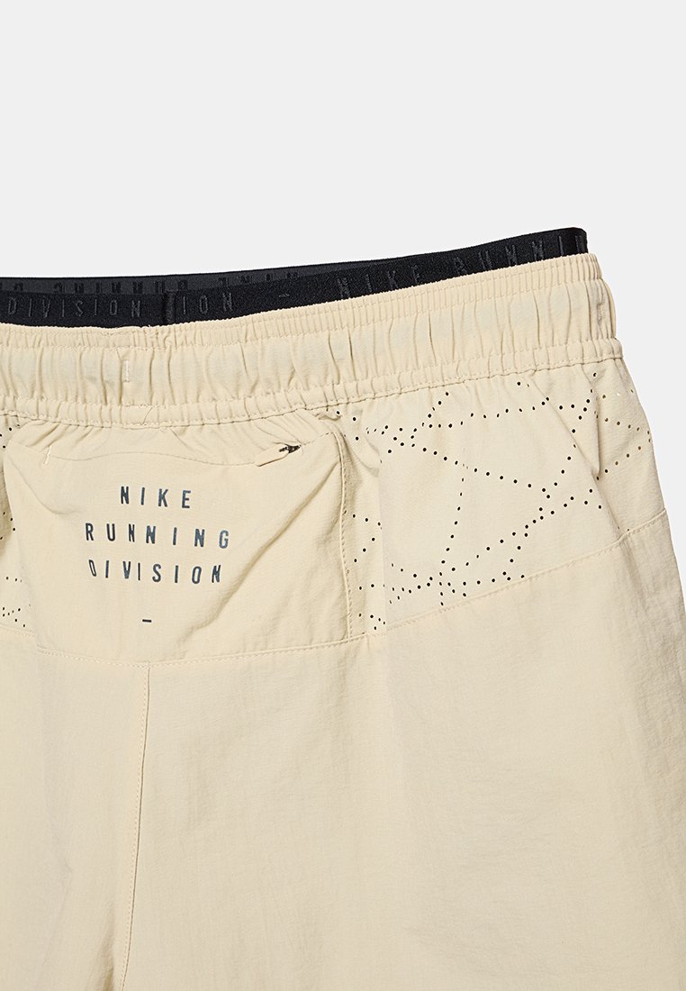 Pantalones cortos de running Nike beige con una cinturilla elástica negra. Incluye un bolsillo de malla y detalles perforados en los lados.