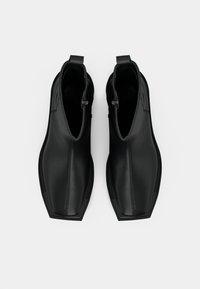 Μαύρα μποτάκια αστραγάλου από λείο δέρμα με στρογγυλεμένη μύτη, ελαστικές πλαϊνές πιέτες και θηλιές για να φοριούνται εύκολα. Μινιμαλιστικός σχεδιασμός με κομψό, γυαλιστερό φινίρισμα.