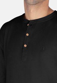 Schwarzes Langarm-Henley-Shirt aus glattem Stoff, mit einer Knopfleiste mit zwei Holzknöpfen und einem dezenten Logo.