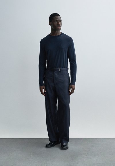 Μπλε πουκάμισο με μακριά μανίκια και παντελόνι με λεπτές ρίγες και ζώνη. Ομαλή υφή υφάσματος, άνετη εφαρμογή, και μαύρα παπούτσια ολοκληρώνουν την εμφάνιση.