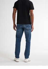 Camiseta oscura con cuello redondo, combinada con jeans de mezclilla azul claro. Los jeans tienen un corte recto y dos bolsillos traseros. Zapatillas blancas completan el look.