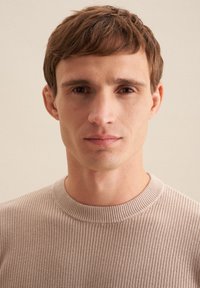 Beige Rippstrickpullover mit rundem Ausschnitt, strukturiertem Material und subtilen horizontalen Mustern, getragen von einem männlichen Modell vor einem neutralen Hintergrund.