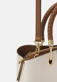 Sac fourre-tout synthétique beige avec des poignées tressées marron, quincaillerie dorée et fermeture à zipper. L'intérieur est équipé d'une doublure marron foncé.
