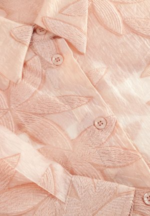 Pale pink shirt featuring floral embroidery, a collared neckline, and light, textured fabric with button closures.