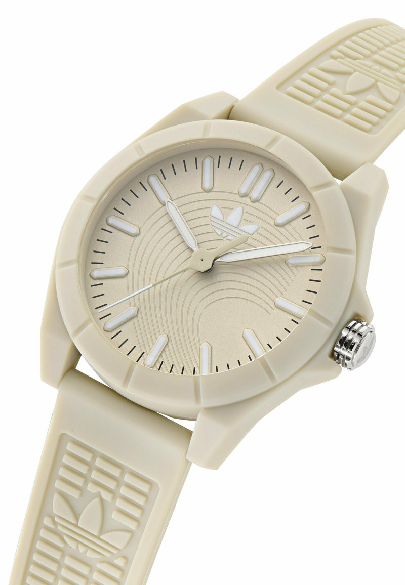 Montre en plastique beige avec un cadran rond, un cadran texturé, des marqueurs d'heure blancs et un logo à 6 heures. Bracelet en silicone lisse avec des accents de motif.