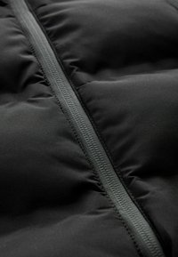 Tissu noir matelassé avec une fermeture éclair verticale centrale étanche, montrant les détails des coutures et de la texture.
