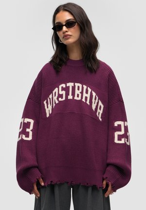 Oversized purple sweater with white text "WRSTBHVA" and "23" on sleeves, ribbed texture, and distressed hem.