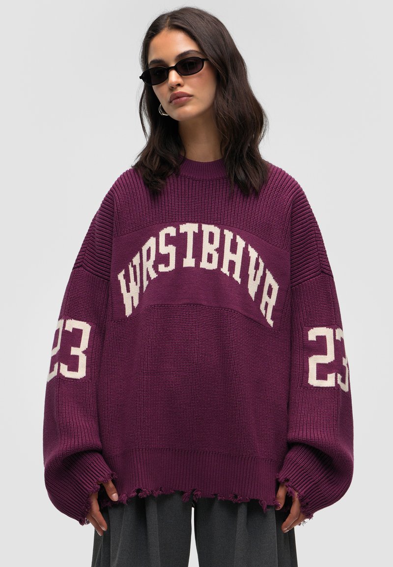 Übergroßer lila Pullover mit weißem Text "WRSTBHVA" und "23" an den Ärmeln, geripptem Muster und ausgefranstem Saum.