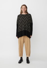 Zwart en beige chevronpatroon oversized trui met lange mouwen, gecombineerd met beige broek en zwarte instappers. Gladde textuur en relaxte pasvorm.