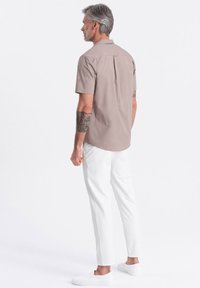 Helles beige Kurzarmhemd mit geradem Schnitt, Rückenfalte und weißen Slim-Fit-Hosen. Graue Slipper vervollständigen das Outfit.