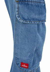 Blaue Jeans-Arbeitsanzughose mit lockerer Passform, ausgestattet mit einem roten Logo-Patch, einer Cargotasche und kontrastierenden orangefarbenen Nähten.