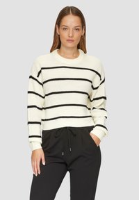Crème trui met zwarte horizontale strepen, ribbelstructuur en een ronde halslijn. Gecombineerd met zwarte broek met een elastische tailleband.