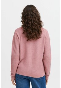 Pull rose pâle à manches longues, avec un ourlet et des poignets côtelés, en matière douce et duveteuse, porté sur un jean bleu. La vue de dos montre un tissu texturé.