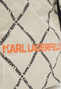 Torba na zakupy z płótna z kremowym tłem, powtórzonym czarnym tekstem "KARL LAGERFELD" oraz wyrazistym pomarańczowym logo. Teksturowany materiał z trwałym szwem.