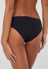 Slip bikini nero con una texture liscia, design a vita alta e a media altezza, che mette in evidenza cuciture minime e una finitura elegante.