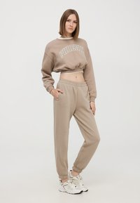 Przycięty beżowy sweatshirt z napisem "PHOENIX", w połączeniu z pasującymi beżowymi dresami. Miękka tekstura, elastyczne mankiety i kieszenie boczne.