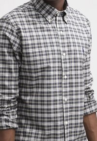 Camisa de botones con un patrón de cuadros en colores azul, verde y blanco, con cuello y mangas arremangadas. Textura de tela suave.