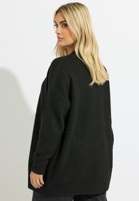 Svart stickad kofta med ett texturerat mönster, oversized design, långa ärmar, sidofickor och avslappnad passform, lämplig för lager på lager.