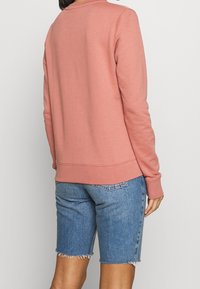 Felpa rosa con maniche lunghe e polsini a costine, abbinata a pantaloni shorts di jeans chiari con orlo sfrangiato.