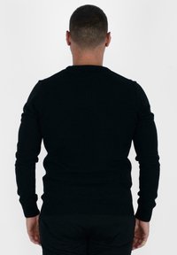 Maglione nero a maglia con maniche lunghe, scollatura rotonda, orlo e dettagli dei polsini a coste. Design semplice e aderente con texture morbida.