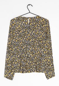 Blouse noire à fleurs avec manches longues, présentant des fleurs jaunes et blanches, taille froncée et détail de dos en clé, fabriquée à partir d'un tissu léger.