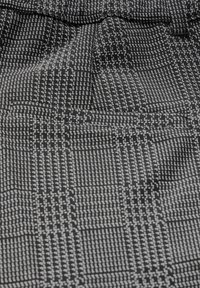 Mustavalkoinen kuvioitu kangas, jossa on ruudullinen malli ja tekstuuriset viivat, jotka korostavat kudottua ilmettä ja vaihtelevia sävyjä kontrastina.