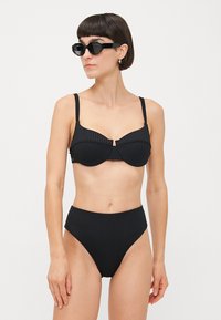 Schwarzes Bikini-Set mit gerippter Textur, Unterdrahtunterstützung und hochgeschnittenen Höschen. Accessoriert mit kantigen schwarzen Sonnenbrillen.