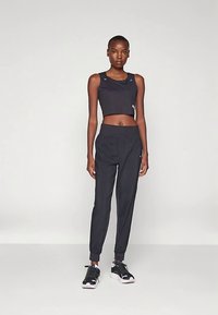 Svart atletisk croptop med ribbad struktur, kombinerad med avsmalnande svarta joggers och svarta sneakers med rosa detaljer. Silhuetten är figurnära.