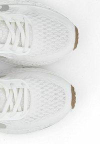 Witte sportschoenen met een gestructureerde mesh bovenkant, platte veters en een lichtbruine rubberen zool. Beschikt over een slank ontwerp en minimale branding.