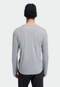 Long-sleeve gray shirt with a textured finish, round neckline, and side slits, paired with a black knit beanie, worn backwards.
