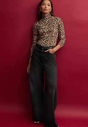 Halenka s dlouhým rukávem v leopardím vzoru s vysokým límcem, spárovaná s širokými černými džíny. Oblečení má texturovaný povrch a elegantní opasek.