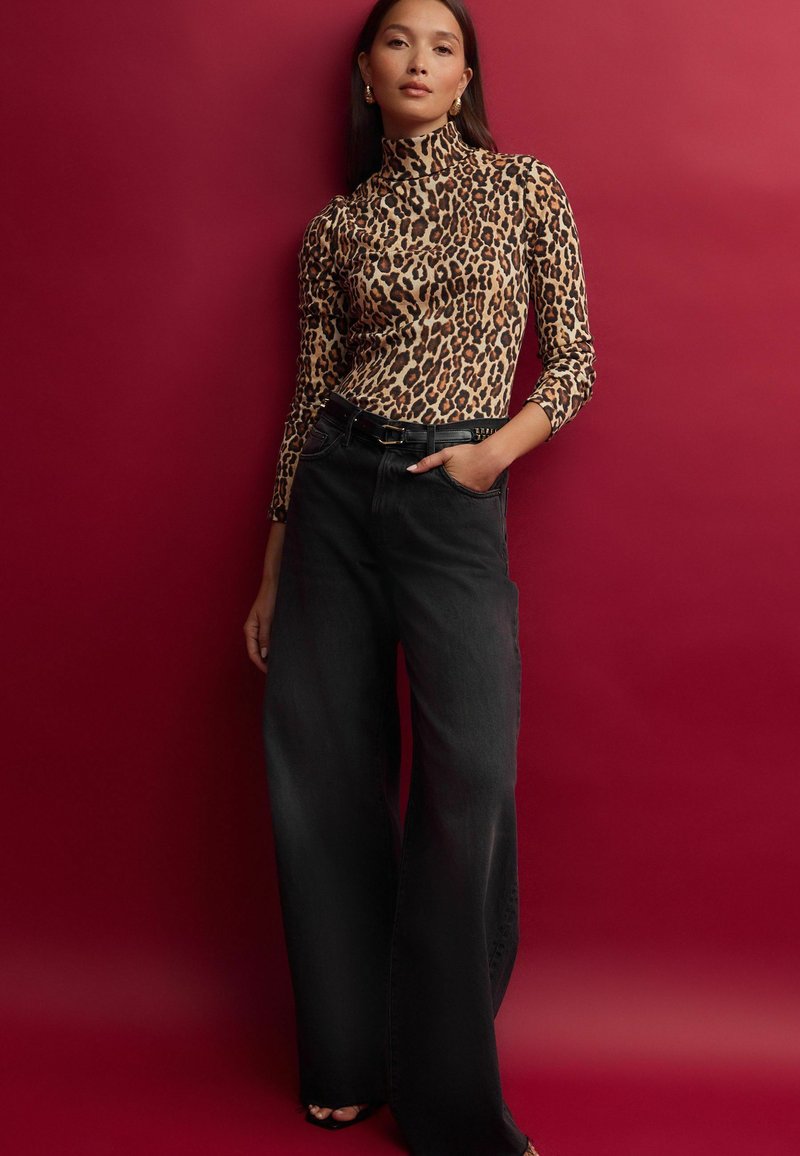 Halenka s dlouhým rukávem v leopardím vzoru s vysokým límcem, spárovaná s širokými černými džíny. Oblečení má texturovaný povrch a elegantní opasek.