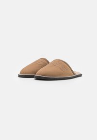 Chaussons en suède marron à enfiler, présentant une forme arrondie, une doublure intérieure douce et un détail de surpiqûre contrastante le long de la semelle noire.