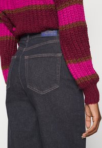 Mörka jeans i denim har hög midja, diskreta bakfickor och kontrasterande sömmar. Bärs tillsammans med en stickad tröja i rosa och vinrött.