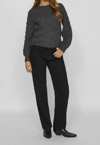 Pull gris tricoté à texture côtelée avec manches volumineuses, associé à un pantalon noir à jambes droites et des bottines noires.