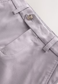 Țesătură gri deschis cu o textură netedă, având un buzunar lateral, față plată și închidere cu nasture. Cusături curate și fără modele vizibile.