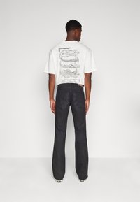 Camiseta blanca de manga corta con estampado gráfico en la parte posterior, combinada con jeans negros de campana, que presentan un diseño simple y detalles de costura.