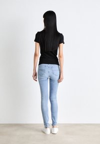 Top negro ajustado de manga corta combinado con jeans skinny de color azul claro. La modelo lleva puestos zapatos blancos. Tejido suave y diseño limpio con un minimalismo en los detalles.