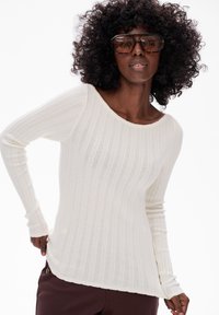 Długi rękaw biały sweter w prążki z szerokim dekoltem i teksturowanym materiałem. Dolna krawędź jest lekko zaokrąglona, z falbaniastym wykończeniem.