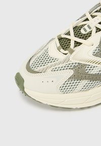 Sneaker med mesh- og syntetisk overdel i krem og oliven, med et strukturert mønster og hvite snørebånd. Tykk såle med grønne aksenter.