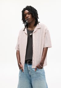 Kortærmet skjorte med knapper i et lyst ternet mønster, parret med en sort mesh tank top og lyseblå vidde denimshorts.