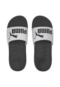 Chanclas en blanco y negro con suela de goma texturizada, que presentan un prominente logo negro de Puma en una tira blanca y un patrón de olas en la plantilla.