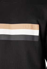 Svart sweatshirt med en horisontell panel med beige, vita och grå ränder. "BOSS" är präglat på det beige området. Texturerat tyg.