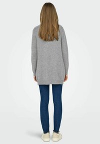 Pull en tricot gris à manches longues, à coupe décontractée, avec un ourlet côtelé, associé à un jean bleu et des chaussures de couleur claire.