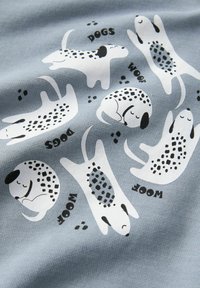 Perros de dibujos animados blancos con manchas negras en varias posturas sobre una tela azul, acompañados de las palabras "PERROS" y "GUAAU" y huellas de patas negras.