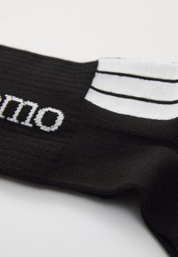Schwarze Socke aus strukturiertem Stoff, mit weißem Streifenmuster am oberen Ende und gesticktem Markennamen in Weiß.